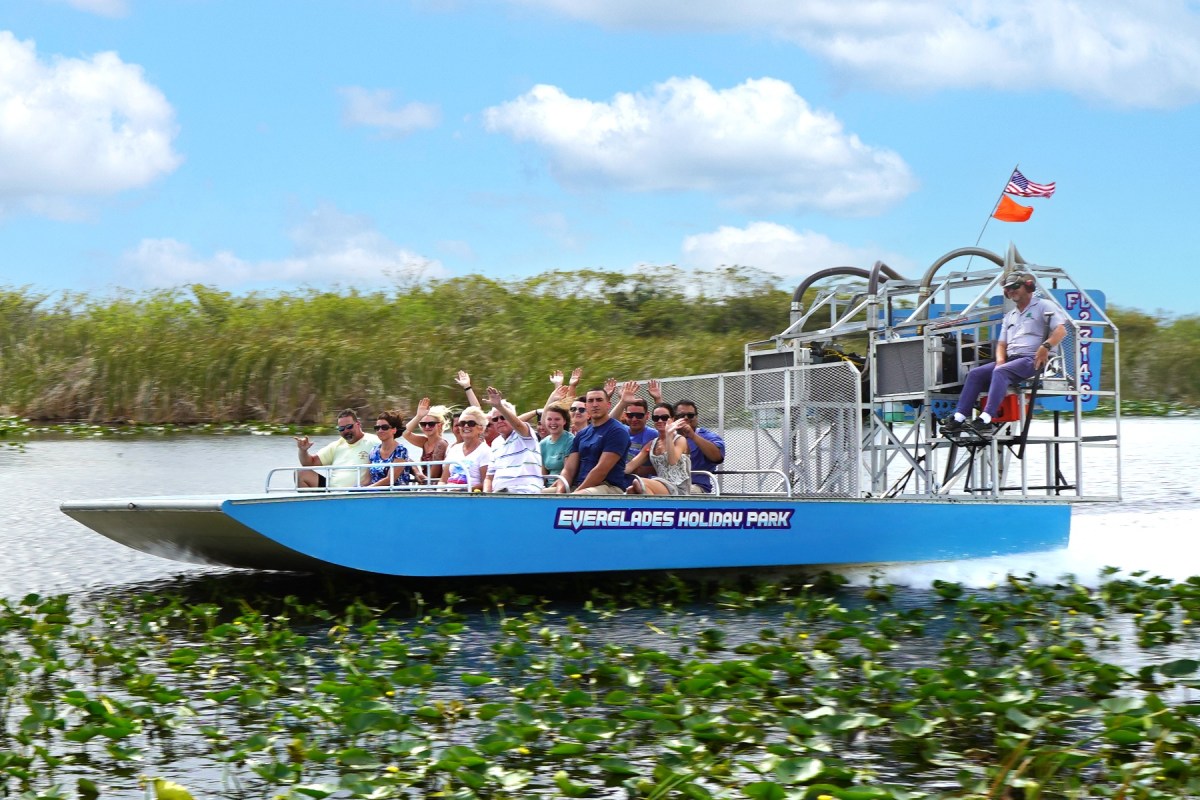 People on an airboat in a marsh, enjoying a ride under a clear sky.