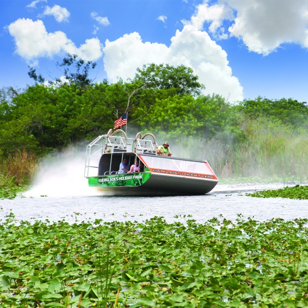 Airboat gliding through a lush green swamp with clouds in the sky.