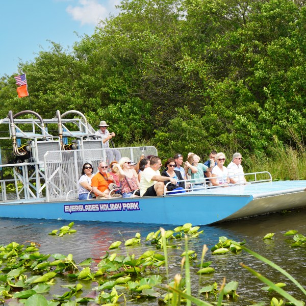 Airboat with passengers tours a lush, green waterway under a clear sky.