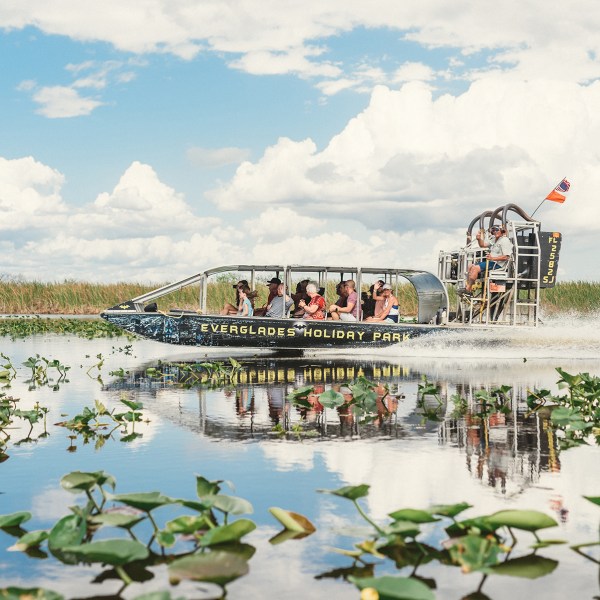 Airboat with tourists glides through Everglades marsh under cloudy sky.