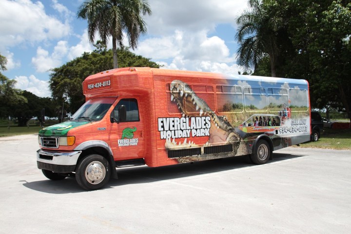 Everglades-themed bus with alligator graphics in a sunny park.