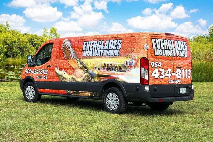 Colorful van with Everglades Holiday Park advertisement, showing a scenic image and contact info.